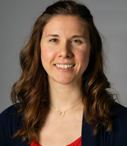 Dr. Tiffany Panko, a white woman with curled brown hair, is in front of a gray background. She wears a necklace with a diamond circle and smiles at the camera. She also wears a red top with a black cardigan.