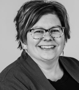 Teresa, a Caucasian woman, appears in a black/white photo. Teresa is wearing glasses, has a bob haircut and is wearing a black cardigan.