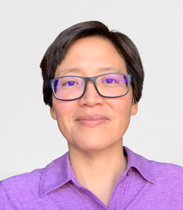 A headshot of an individual who is of Asian descent, with short dark hair and wearing glasses and a purple collared shirt. They are looking directly at the camera with a slight smile.