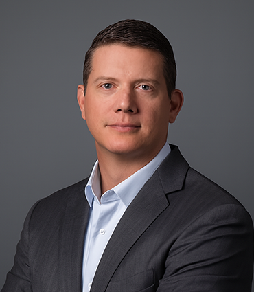 A headshot of William Harkness, who is wearing a suit and light blue shirt, against a dark grey background.