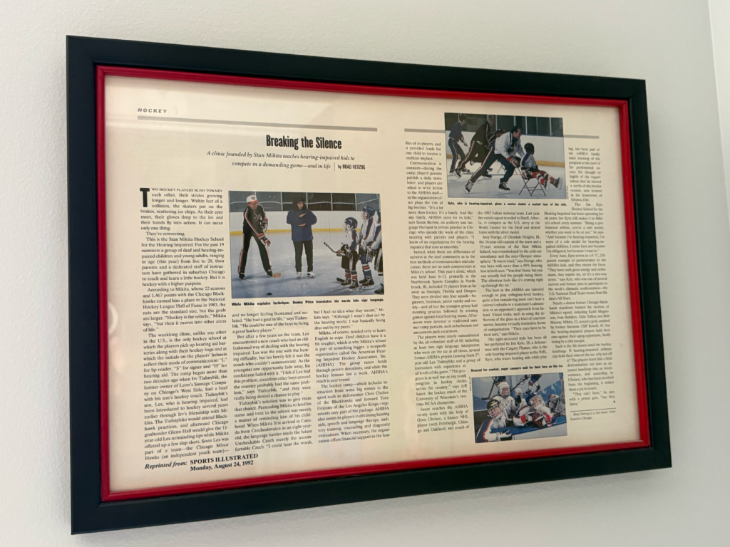 A framed article titled "Breaking the Silence" from Sports Illustrated.jpg features photographs and text about a hockey clinic for Deaf and hard of hearing children founded by Stan Mikita. The display includes several main images of hockey players on the ice alongside several columns of printed journalistic text.